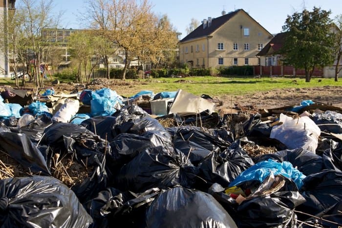 A substantial amount of black bin bags and other household rubbish is illegally fly-tipped across a barren field posing an unsightly environmental problem near residential buildings.