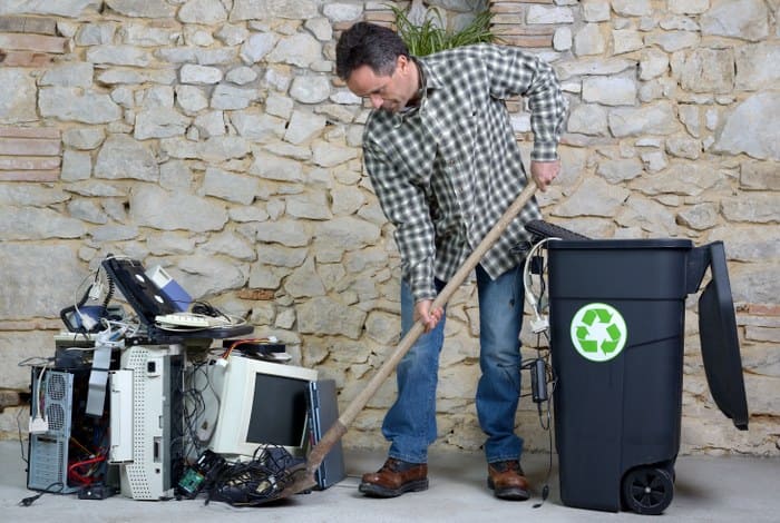 A man diligently shovels a pile of electronic waste into a designated recycling bin highlighting proper rubbish disposal to help solve the fly-tipping problem.